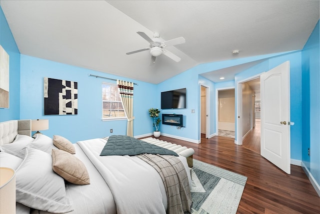 bedroom with lofted ceiling, a ceiling fan, a glass covered fireplace, wood finished floors, and baseboards