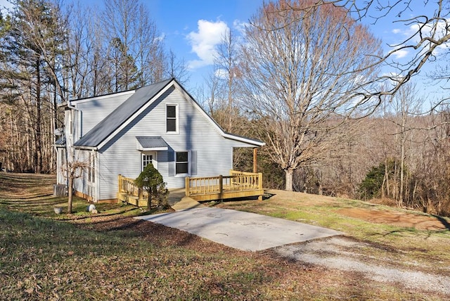 view of side of home featuring driveway, a lawn, and a wooden deck