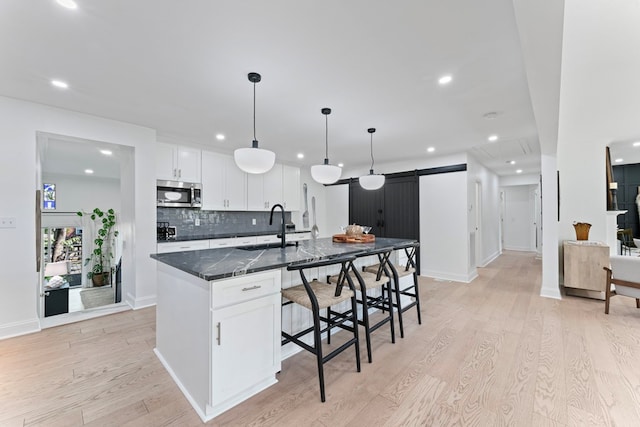 kitchen with a kitchen island with sink, a barn door, stainless steel microwave, and white cabinetry