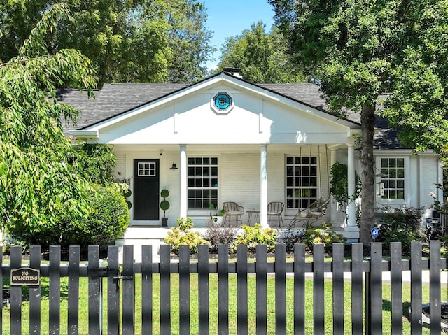 view of front facade featuring covered porch, brick siding, roof with shingles, and a fenced front yard