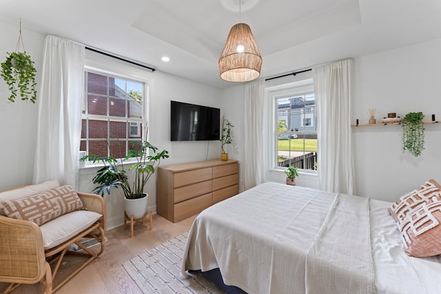 bedroom featuring light wood-type flooring, a raised ceiling, and recessed lighting