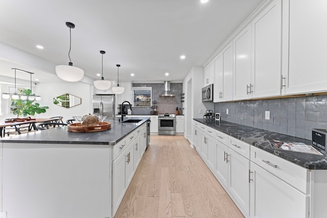 kitchen with stainless steel appliances, wall chimney range hood, white cabinetry, pendant lighting, and a sink