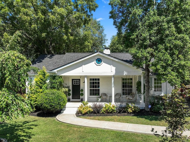 view of front facade featuring covered porch, a shingled roof, a chimney, and a front yard