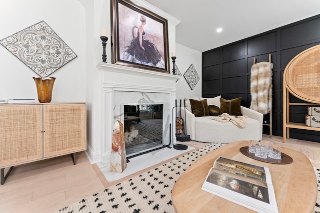 living area featuring light wood-type flooring, a high end fireplace, a decorative wall, and recessed lighting