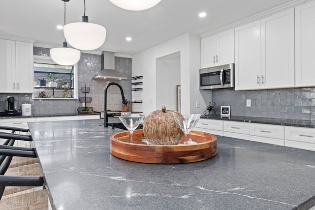 kitchen featuring stainless steel microwave, a large island, wall chimney exhaust hood, and white cabinetry