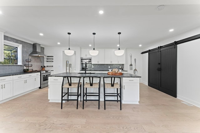 kitchen with a barn door, dark countertops, a spacious island, appliances with stainless steel finishes, and wall chimney range hood