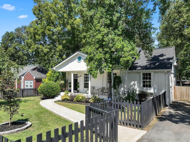 view of front of house with brick siding, a shingled roof, a fenced front yard, covered porch, and a front yard