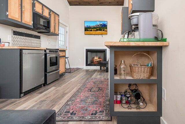 kitchen featuring light countertops, appliances with stainless steel finishes, wood finished floors, a lit fireplace, and baseboards