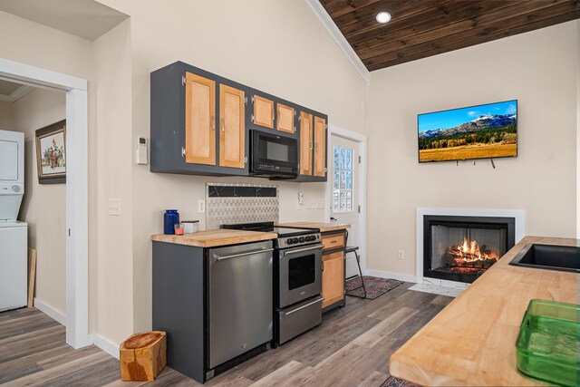 kitchen featuring stainless steel appliances, stacked washer / dryer, butcher block counters, and a fireplace with flush hearth