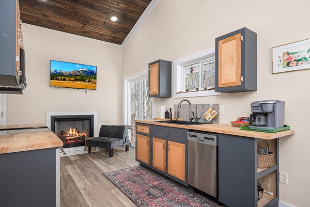 kitchen featuring light wood finished floors, wood counters, a lit fireplace, stainless steel dishwasher, and a sink