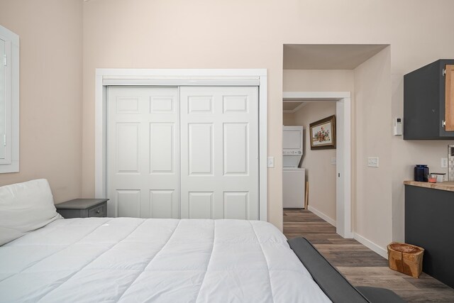 bedroom featuring a closet, stacked washing maching and dryer, dark wood finished floors, and baseboards