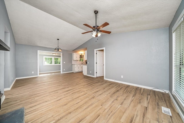 unfurnished living room with visible vents, light wood-style floors, vaulted ceiling, ceiling fan, and baseboards