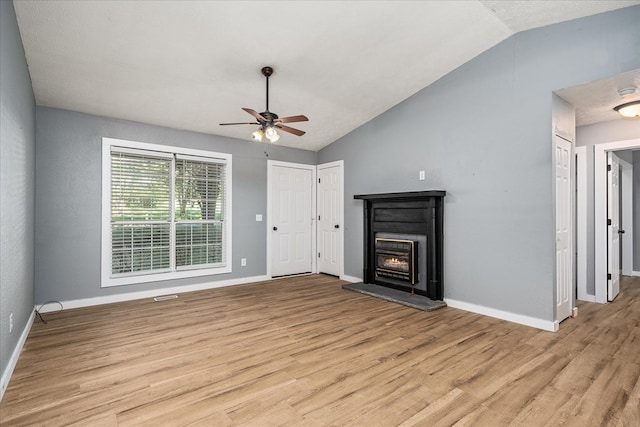 unfurnished living room featuring light wood-type flooring, a lit fireplace, baseboards, and vaulted ceiling