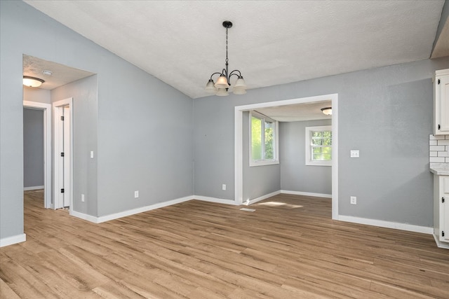 unfurnished dining area featuring light wood-style floors, baseboards, a chandelier, and a textured ceiling