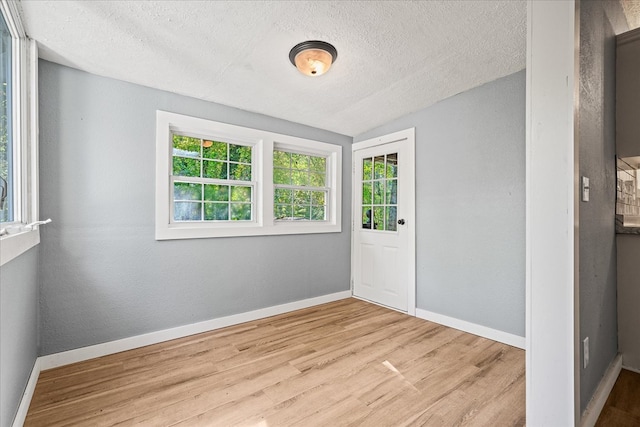 spare room with light wood finished floors, baseboards, a textured wall, lofted ceiling, and a textured ceiling