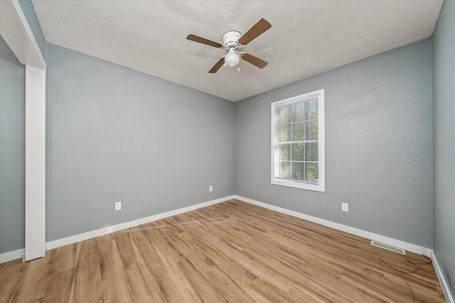 unfurnished room with baseboards, visible vents, light wood finished floors, and a textured ceiling