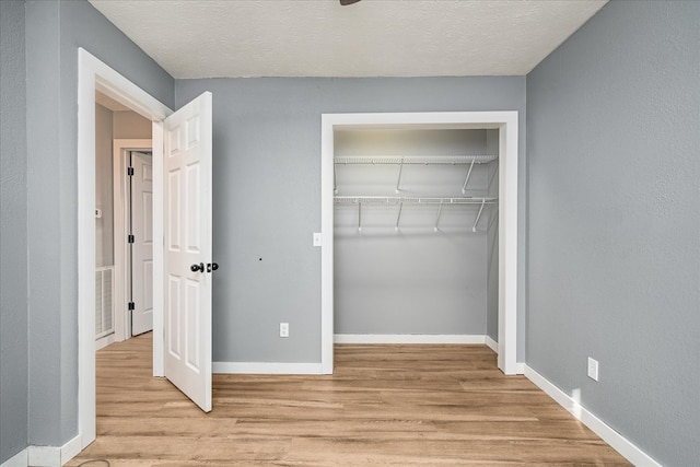 unfurnished bedroom featuring visible vents, baseboards, light wood-style flooring, a textured ceiling, and a closet