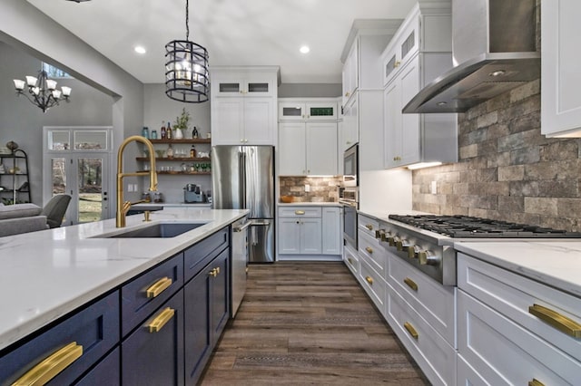 kitchen with stainless steel appliances, glass insert cabinets, white cabinetry, a sink, and wall chimney exhaust hood