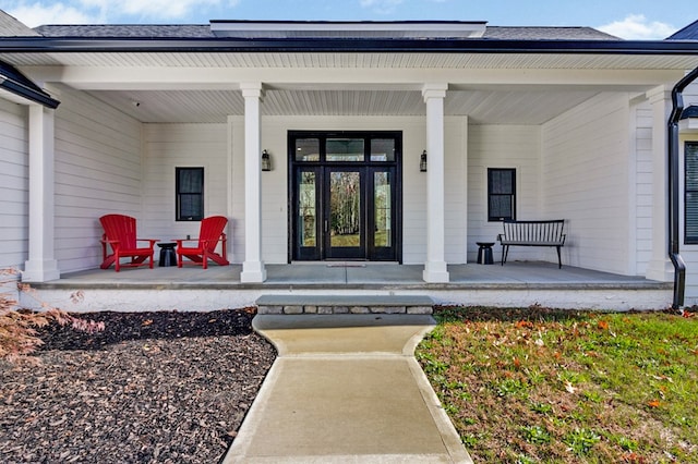 view of exterior entry with covered porch and a shingled roof