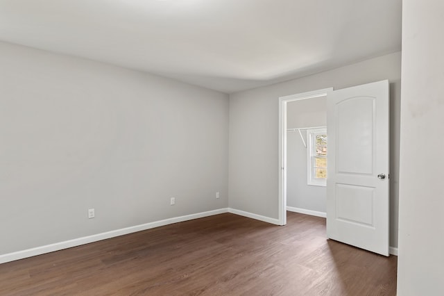 unfurnished bedroom with a walk in closet, baseboards, and dark wood-style flooring