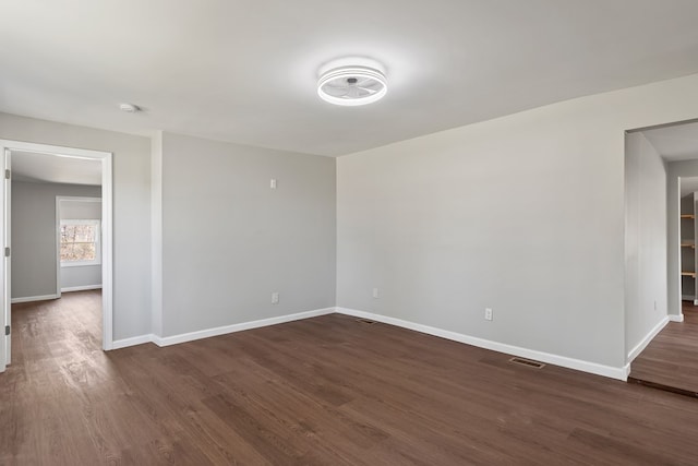 empty room featuring dark wood finished floors, visible vents, and baseboards