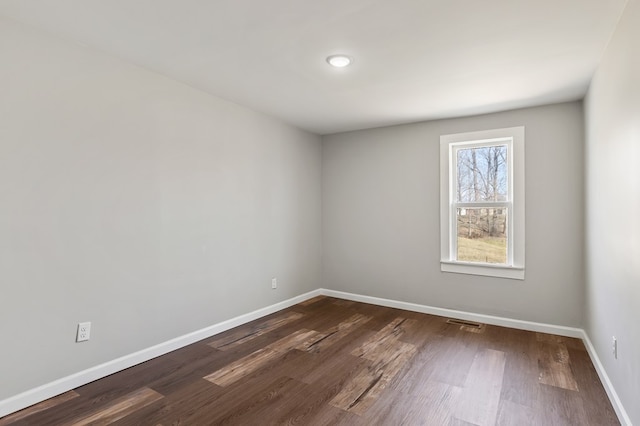 empty room featuring visible vents, baseboards, and dark wood-style flooring