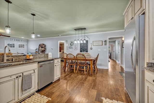 kitchen featuring dark wood-style floors, stainless steel appliances, hanging light fixtures, a sink, and dark stone counters