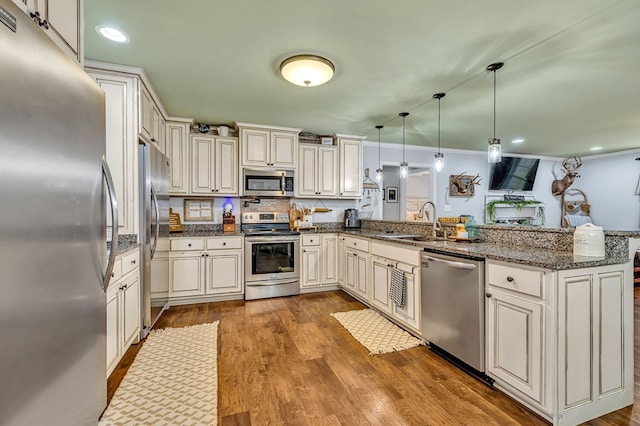 kitchen with a peninsula, appliances with stainless steel finishes, pendant lighting, and a sink