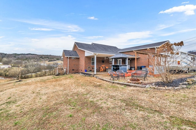 back of house featuring brick siding, a yard, a gazebo, a deck, and a fire pit