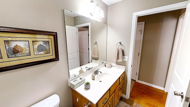 half bath with toilet, baseboards, wood finished floors, and vanity