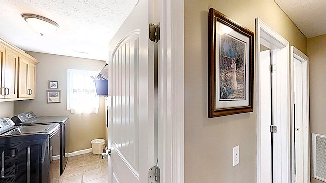 laundry area featuring light tile patterned floors, cabinet space, a textured ceiling, separate washer and dryer, and baseboards