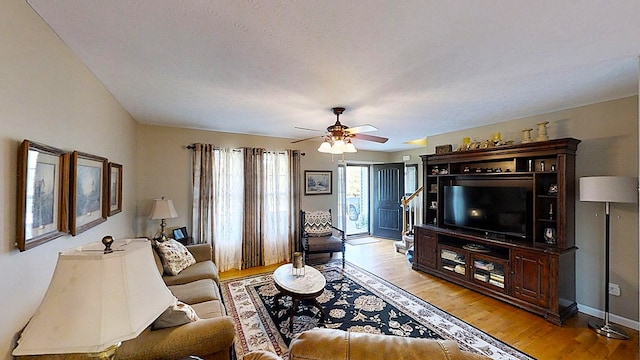 living room featuring light wood-type flooring, a textured ceiling, baseboards, and a ceiling fan