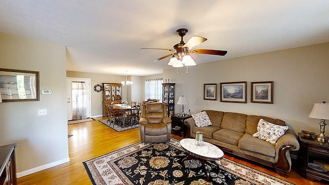 living room featuring light wood-style floors, baseboards, and ceiling fan with notable chandelier