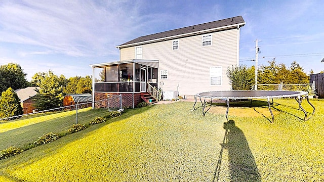 back of house featuring a sunroom, a trampoline, fence, and a yard