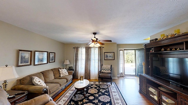 living room with ceiling fan, a textured ceiling, and wood finished floors