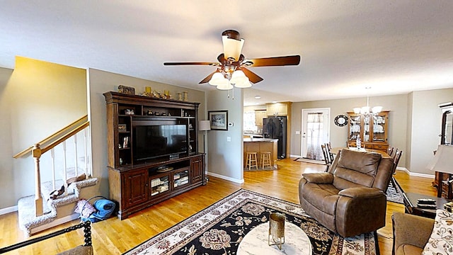 living area with stairs, light wood-type flooring, baseboards, and ceiling fan with notable chandelier