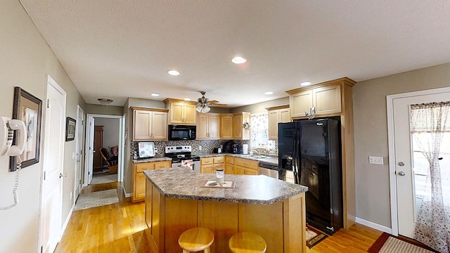 kitchen with dark countertops, a breakfast bar, a center island, a healthy amount of sunlight, and black appliances