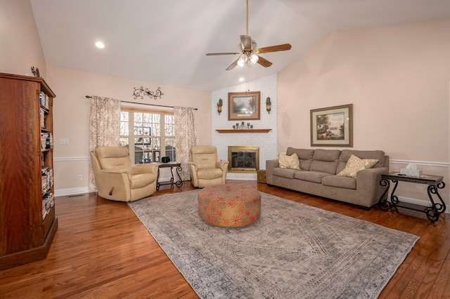 living room with baseboards, dark wood finished floors, a ceiling fan, a brick fireplace, and high vaulted ceiling