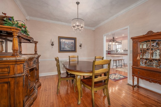 dining room with ornamental molding, baseboards, a notable chandelier, and light wood finished floors