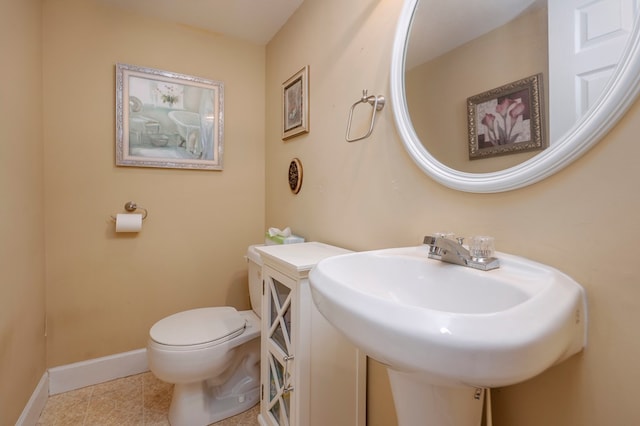 half bath featuring tile patterned flooring, baseboards, a sink, and toilet