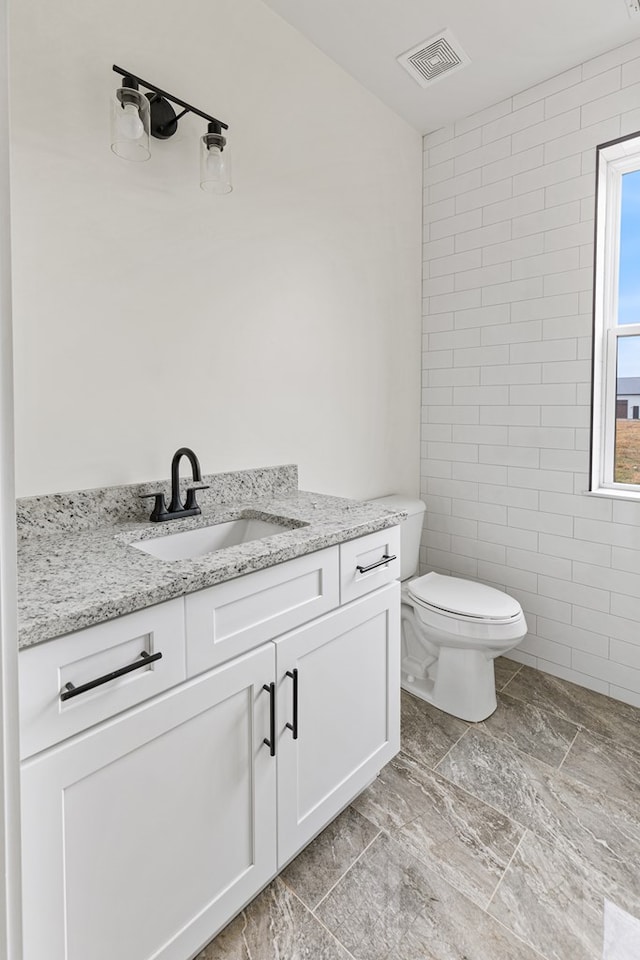 bathroom with toilet, visible vents, tile walls, and vanity