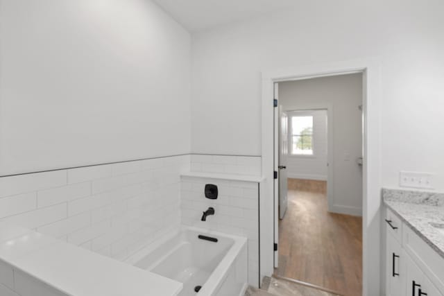 full bathroom with a bathing tub, baseboards, wood finished floors, and vanity