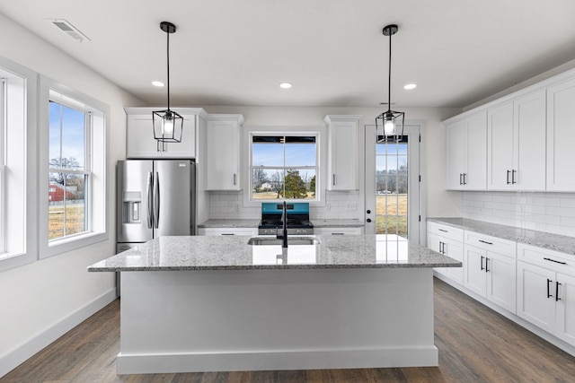 kitchen with light stone counters, hanging light fixtures, white cabinetry, a sink, and an island with sink