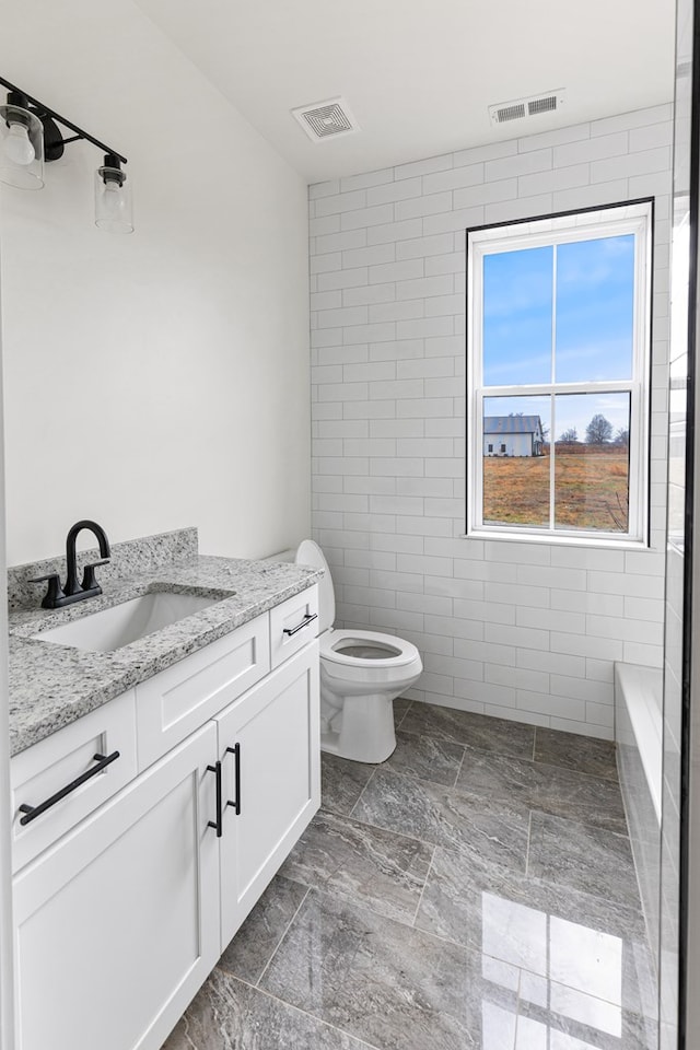 bathroom featuring toilet, vanity, visible vents, and tile walls