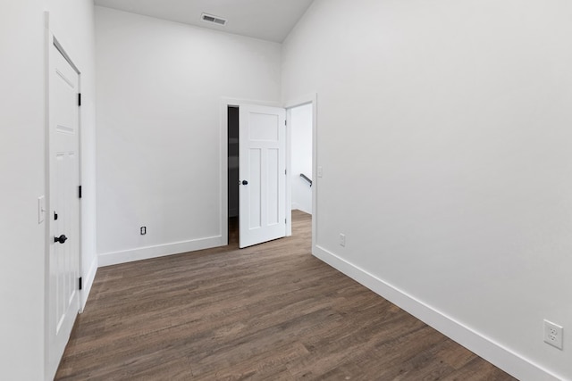 spare room with dark wood-style flooring, visible vents, and baseboards