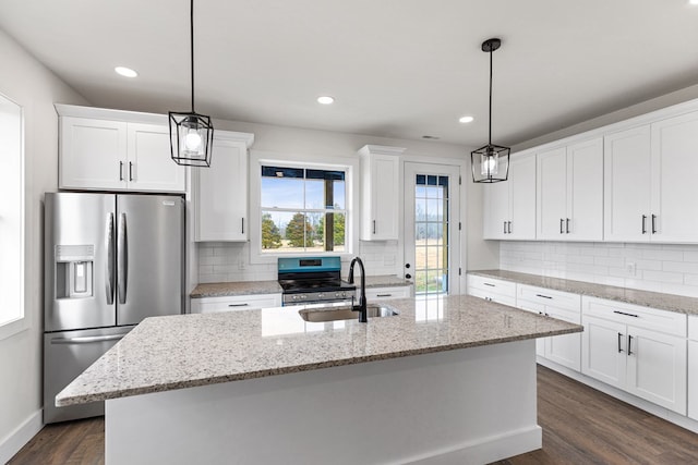 kitchen featuring decorative light fixtures, stainless steel appliances, white cabinets, a kitchen island with sink, and a sink