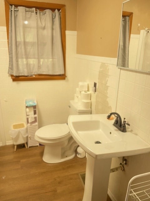 bathroom with toilet, a wainscoted wall, tile walls, and wood finished floors