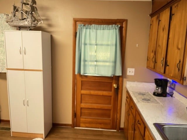 kitchen featuring light countertops, brown cabinetry, a sink, and dark wood finished floors