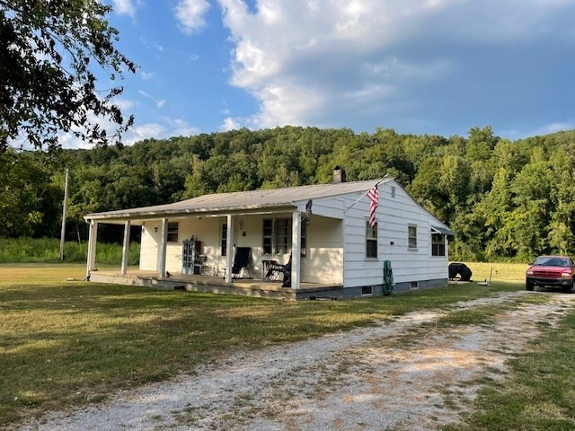 view of front of property featuring covered porch, a front lawn, a chimney, and a view of trees