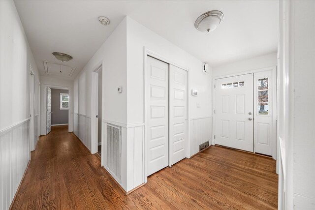 corridor featuring a wainscoted wall, dark wood-style floors, visible vents, and attic access